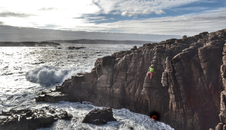 Climber scaling cliff with waves crashing below