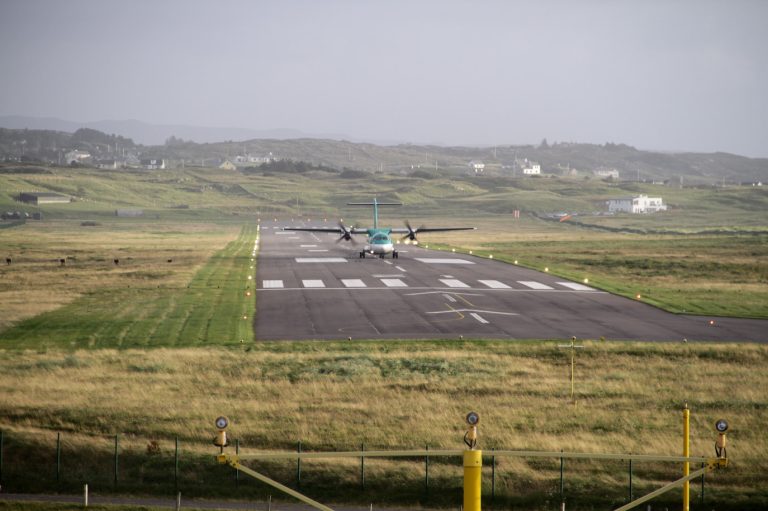 Aer Lingus' ATR-72 taking off down the runway with houses and green hills in the background