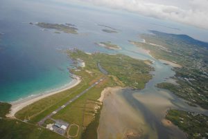 Aerial view of Donegal Airport terminal and runway featuring beaches on either side, islands in the centre and left background and more mainland from the right foreground to the right background.